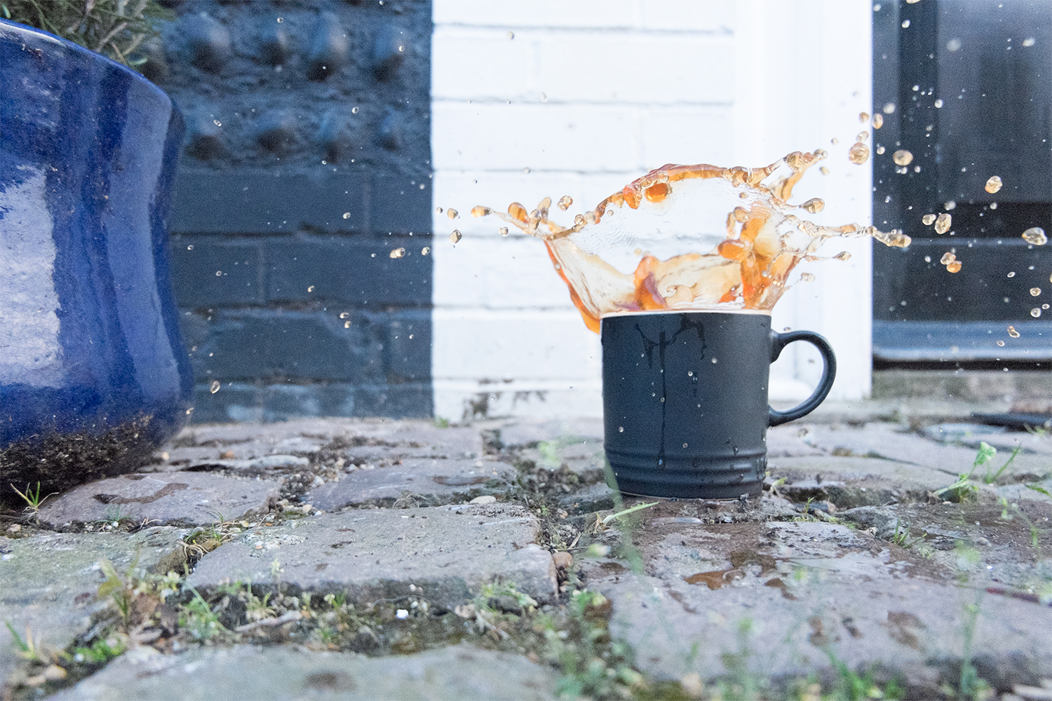 Tea splashing out of a mug, outdoors on a patio. Plant pot on the left.