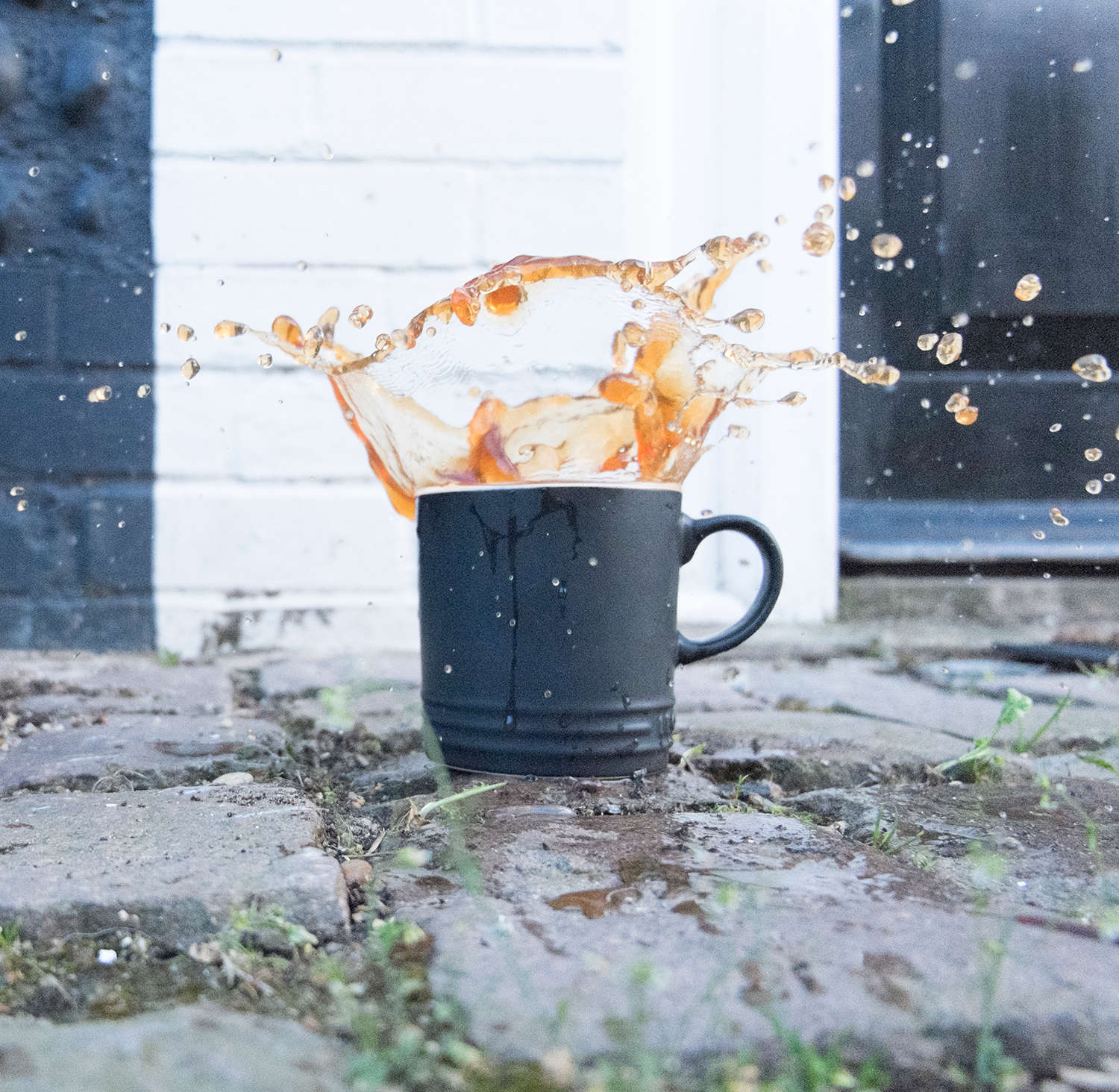 Tea splashing out of a mug, outdoors on a patio. Square crop.