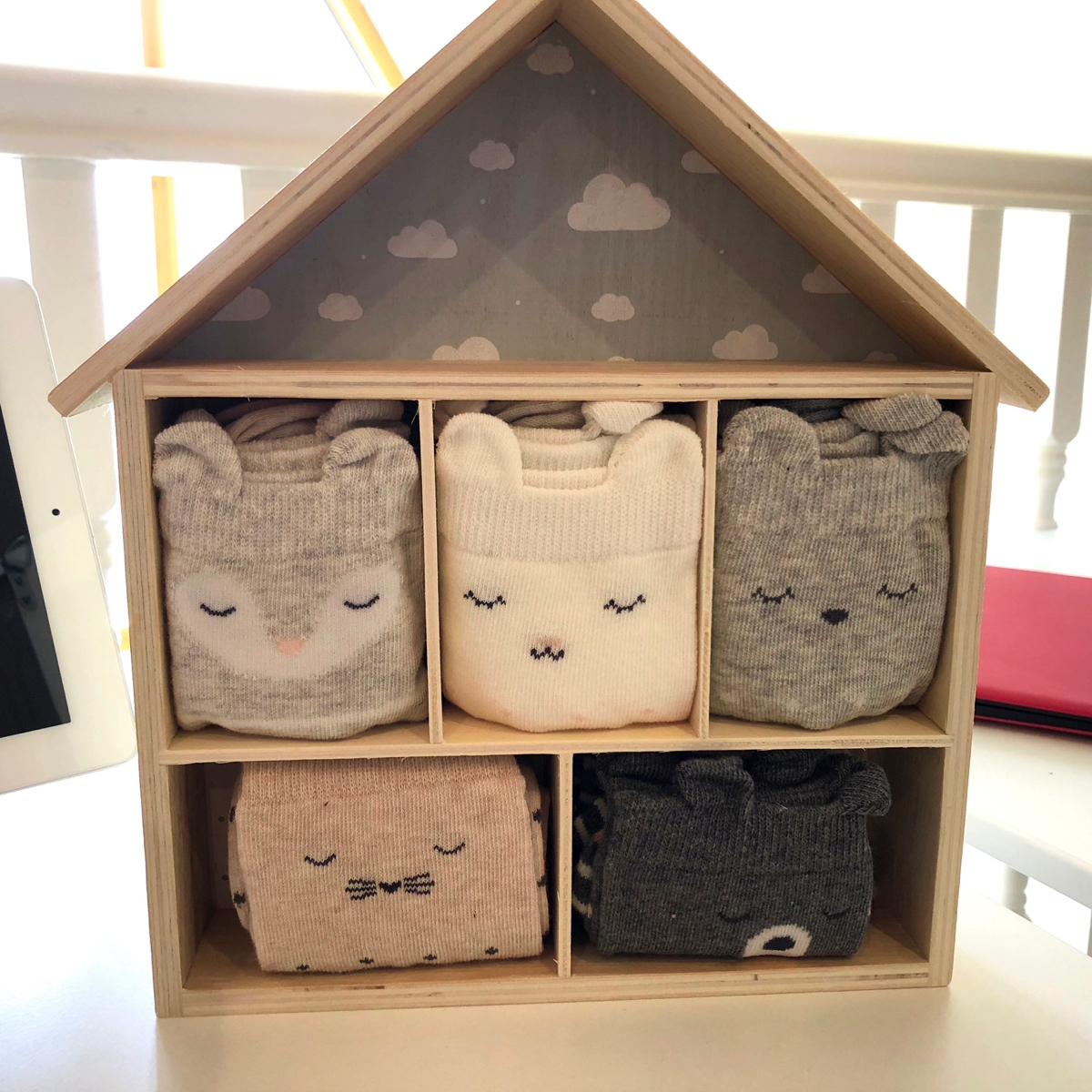 A little wooden shelving unit made to look like a house, containing five pairs of rolled up socks with sleeping animal faces.